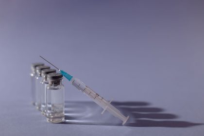 Seringa e frascos de vacina dispostos sobre uma superfície cinza.