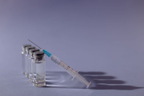 Seringa e frascos de vacina dispostos sobre uma superfície cinza.
