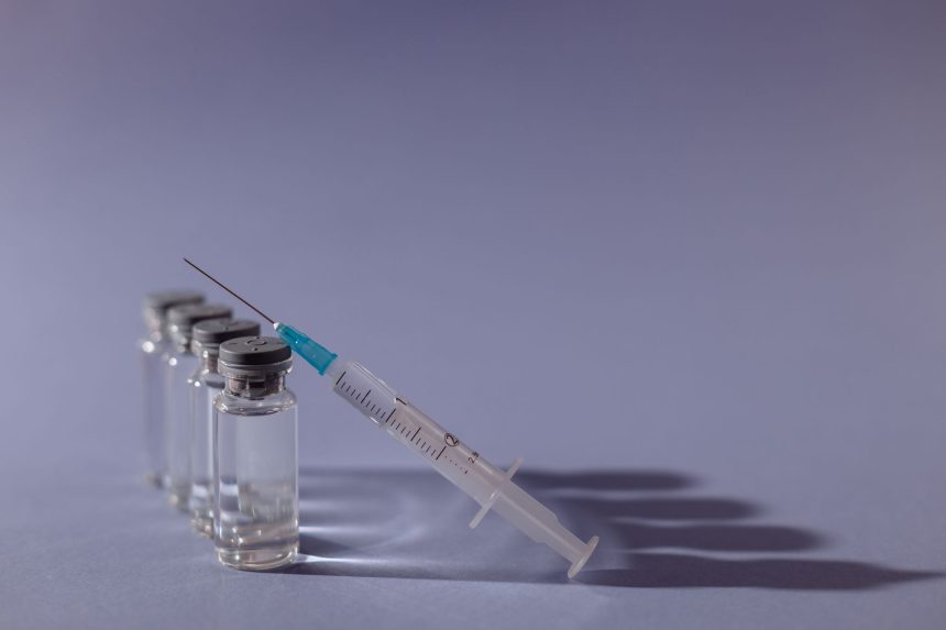 Seringa e frascos de vacina dispostos sobre uma superfície cinza.