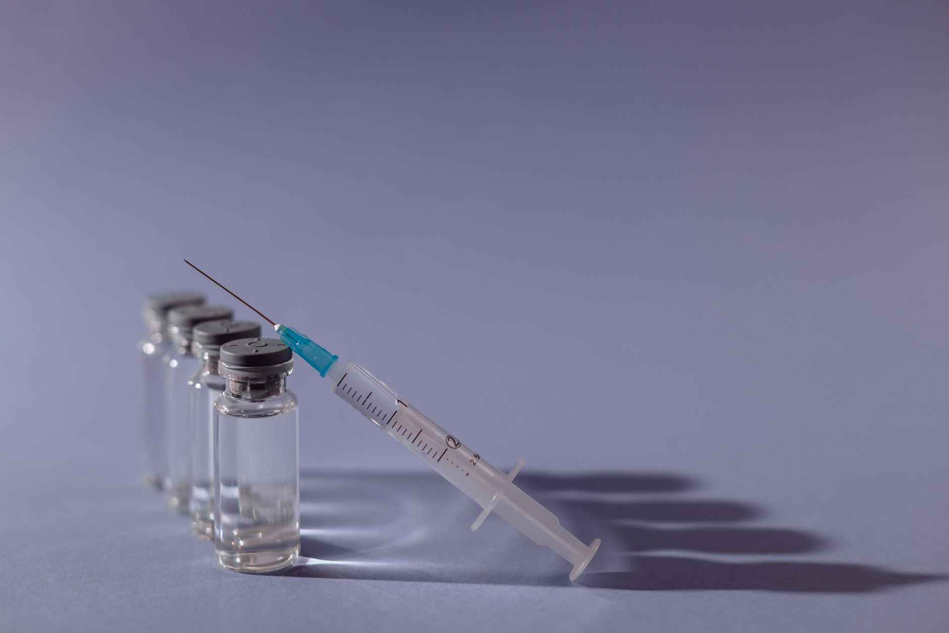 Seringa e frascos de vacina dispostos sobre uma superfície cinza.