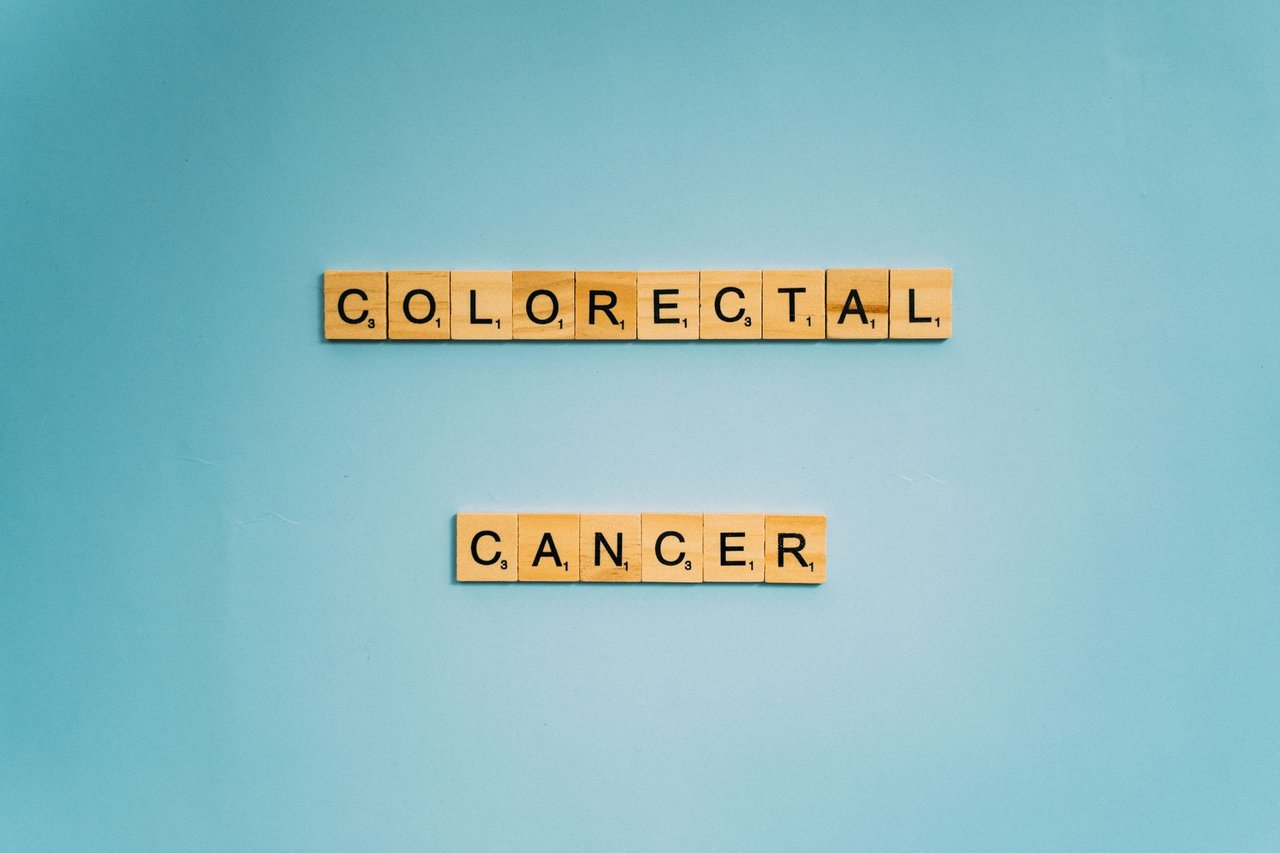 Letras de madeira formam as palavras “Colorectal Cancer” sobre fundo azul claro.
