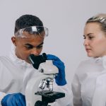 Dois cientistas de jaleco analisam amostras ao microscópio em um laboratório.
