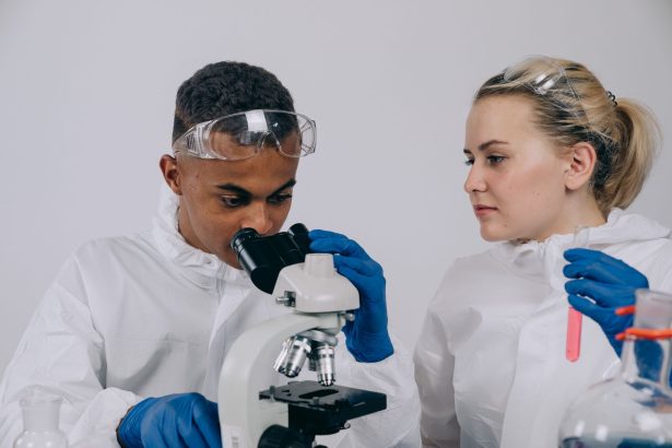 Dois cientistas de jaleco analisam amostras ao microscópio em um laboratório.