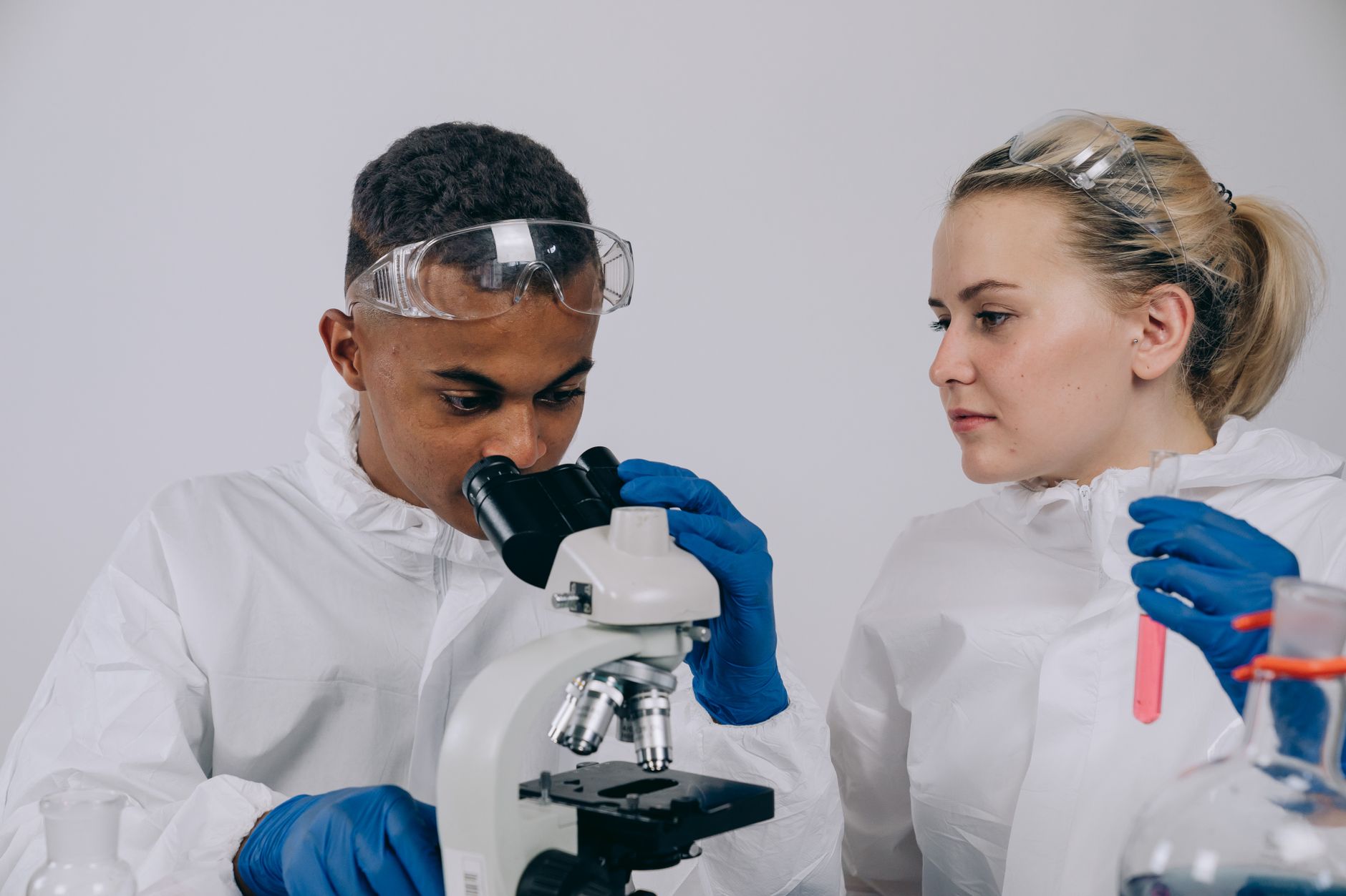 Dois cientistas de jaleco analisam amostras ao microscópio em um laboratório.